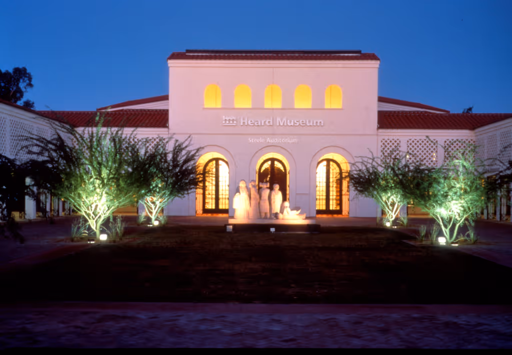 Heard Museum building lit up at dusk with illuminated trees and sculptures in front.